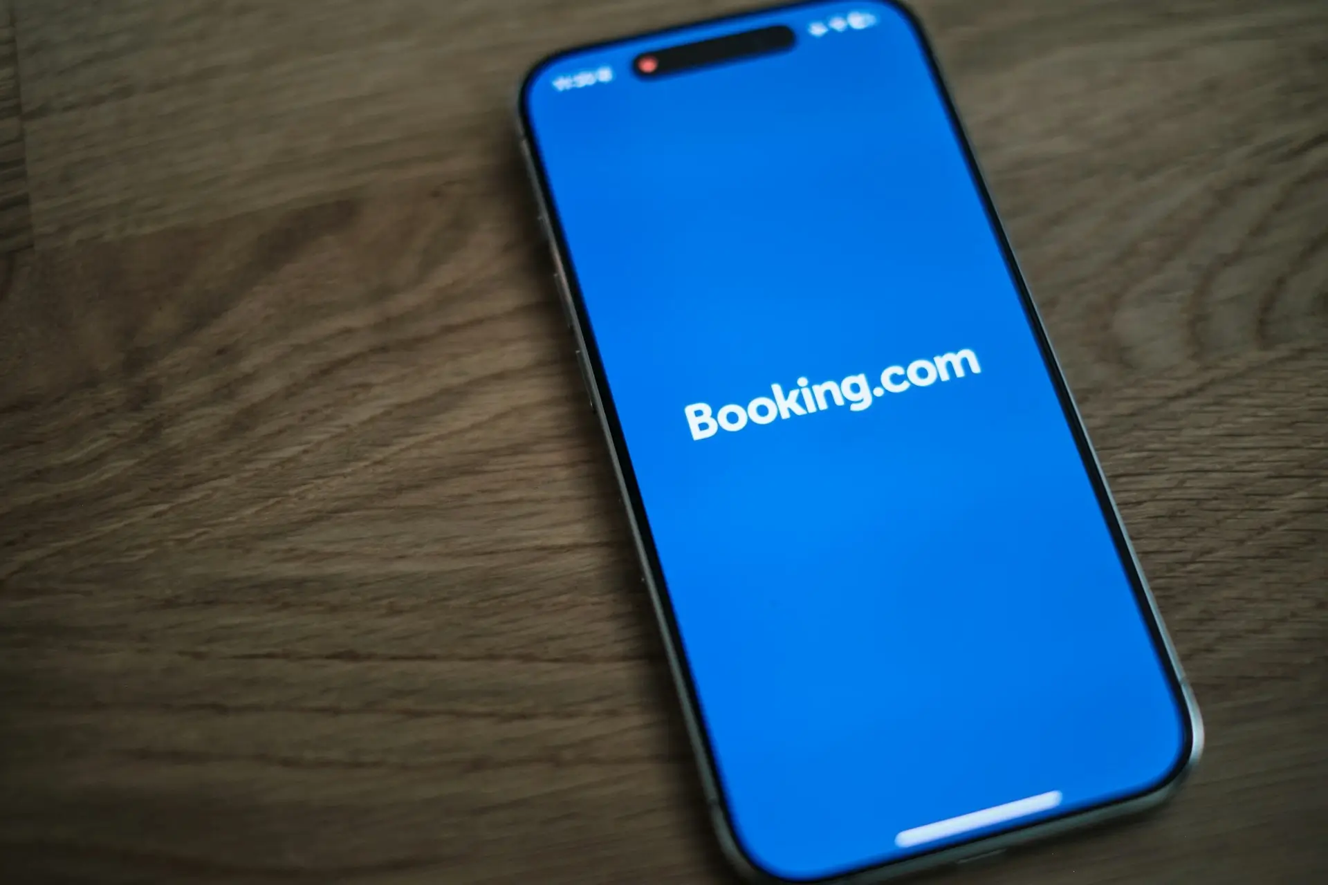 Smartfon leżący na drewnianym blacie z włączoną aplikacją Booking.com wyświetlaną na ekranie.