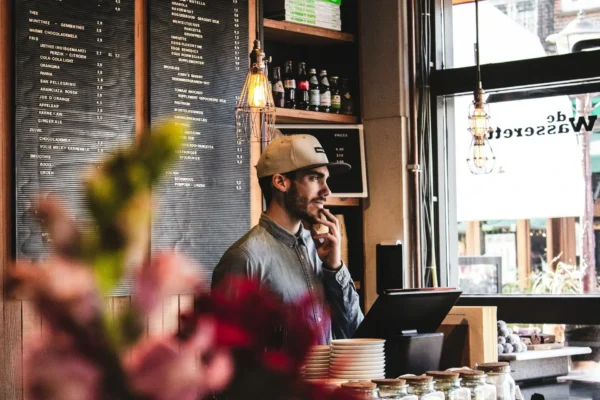 Młody pracownik z uśmiechem stoi za ladą kawiarni.