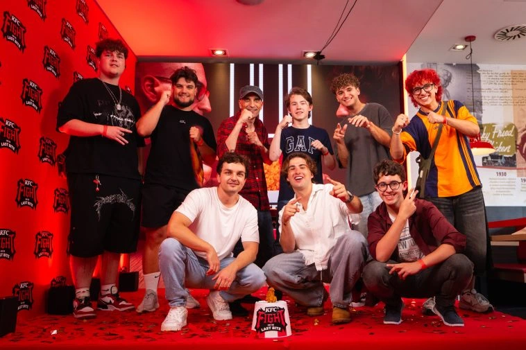 Grupa młodych mężczyzn pozuje do zdjęcia na czerwonym dywanie na tle ścian z logo "KFC Fight for the Last Bite".