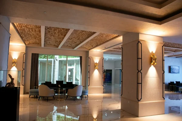 Eleganckie wnętrze hotelowego lobby z marmurową podłogą, nowoczesnym oświetleniem na kolumnach, sufitem z ceglanej mozaiki oraz strefą wypoczynkową z fotelami i stolikami.