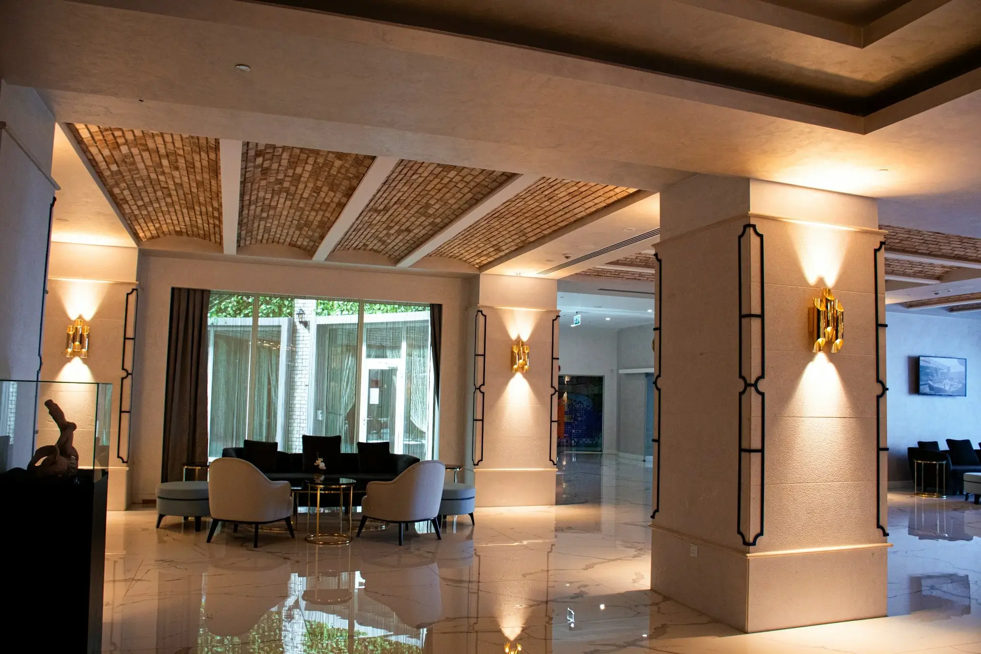 Eleganckie wnętrze hotelowego lobby z marmurową podłogą, nowoczesnym oświetleniem na kolumnach, sufitem z ceglanej mozaiki oraz strefą wypoczynkową z fotelami i stolikami.